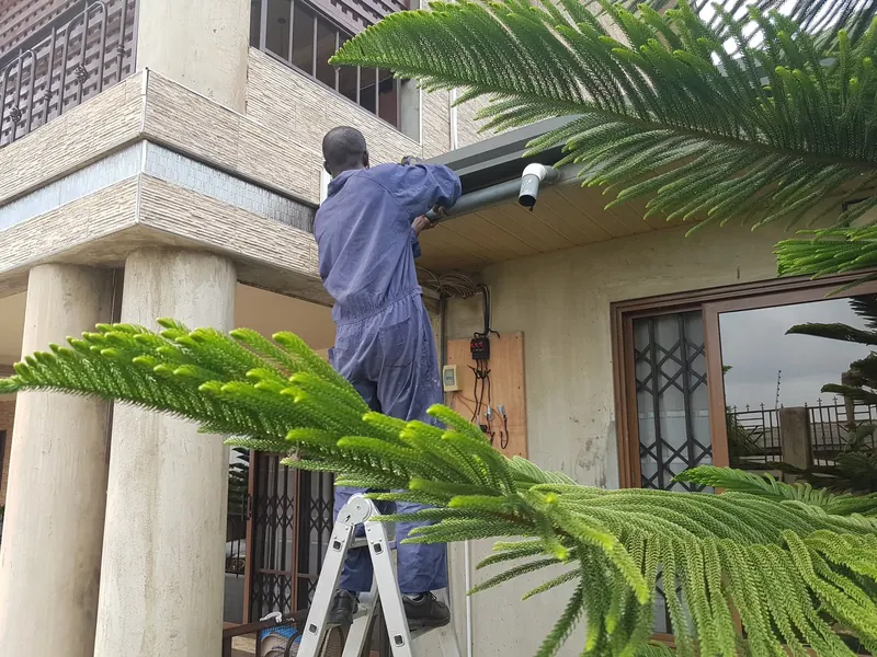 Technician fitting gutter and downpipe brackets on a two-storey house