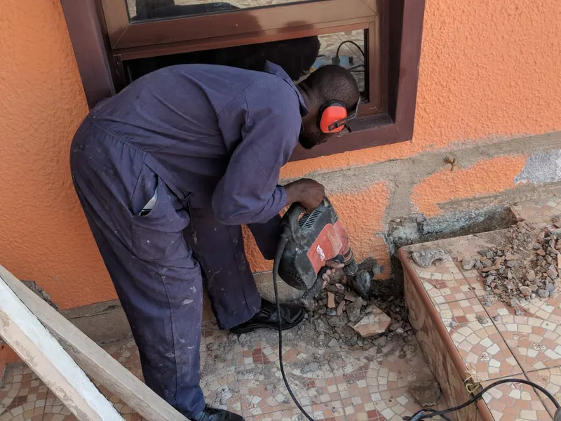 ASAP Plumbing technician in overalls and ear protection cutting a tiled floor to access pipework