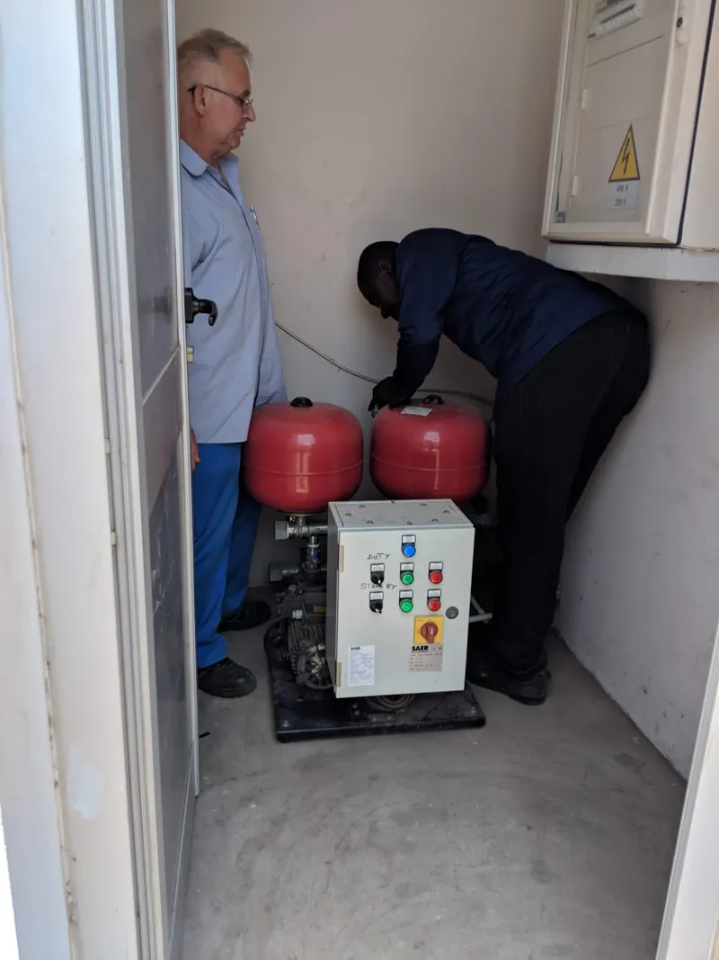 Technician commissioning a booster pump and control panel inside a pump room