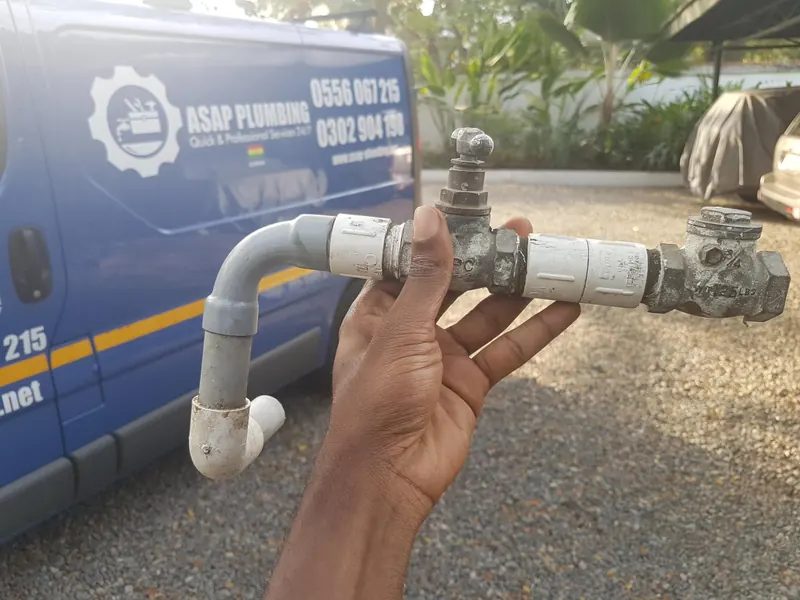 A removed supply valve assembly held up in front of an ASAP Plumbing van